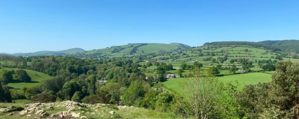 Panoramic view of Welsh countryside on a sunny day, rolling green hills and blue sky
